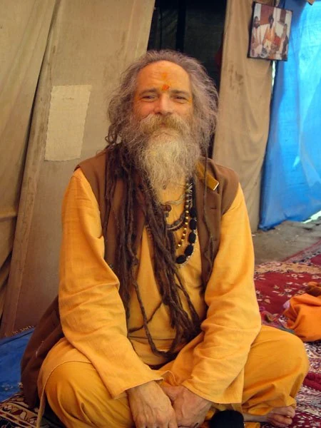 Goa Gil seated and smiling in a sadhu camp, his dreadlocks over one shoulder